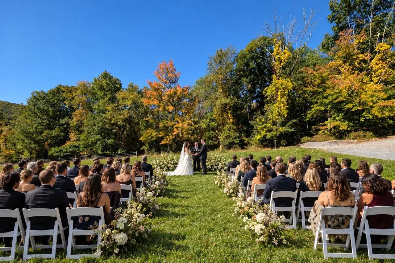 Guests seated on the lawn for an outdoor ceremony with fall trees behind