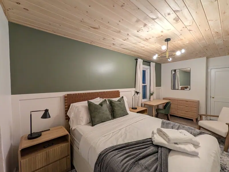 Bedroom 1 welcomes you with a plush queen bed, sage-green walls and crisp white linens.